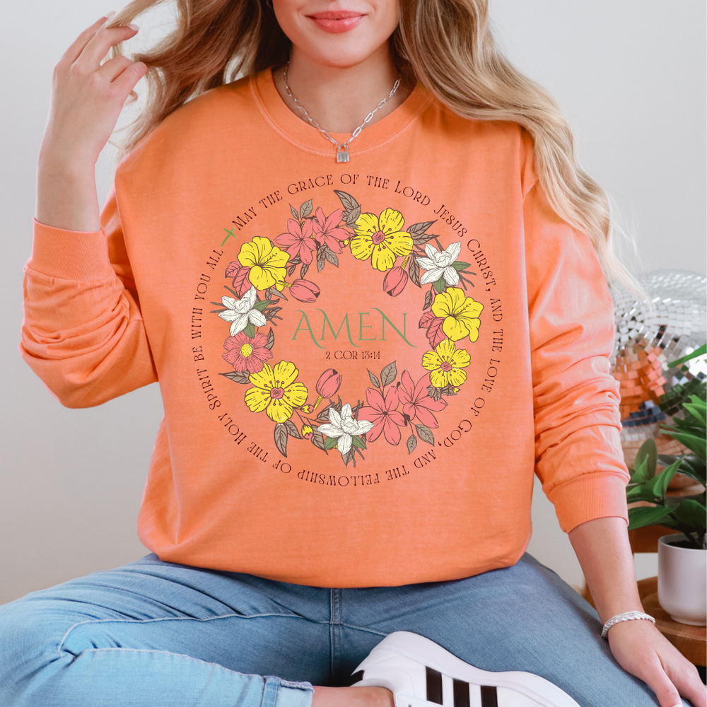 Person in light blue jeans and white sneakers wears an Amen Long Sleeve Tee featuring a floral wreath and biblical verse, embodying Faith Family Designs' unique style.