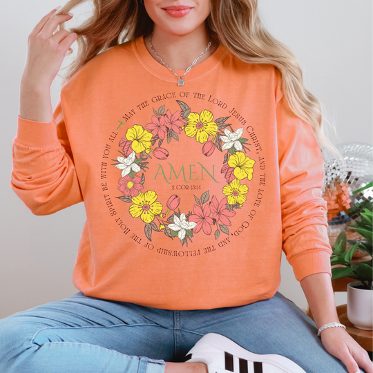 Person in light blue jeans and white sneakers wears an Amen Long Sleeve Tee featuring a floral wreath and biblical verse, embodying Faith Family Designs' unique style.