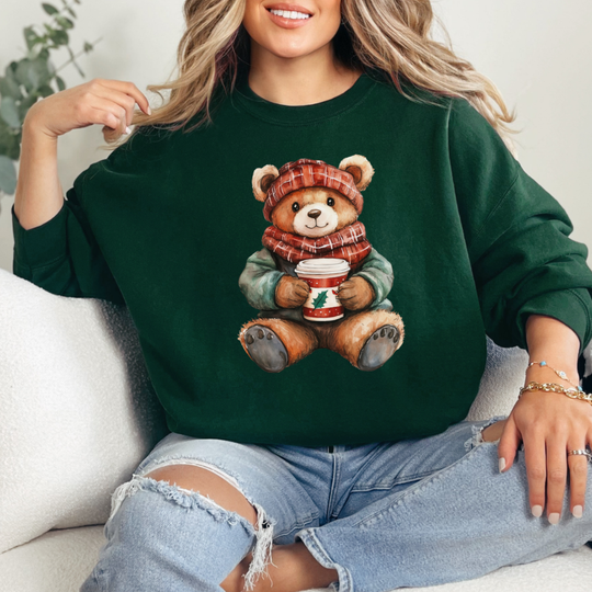 Person wearing the Old Money Bear Crew sweatshirt featuring a teddy bear with a red hat and scarf, holding a holiday coffee cup, paired with ripped jeans.