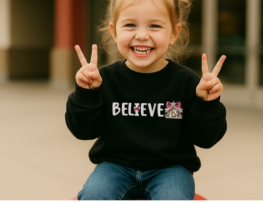 Child wearing BELIEVE toddler sweatshirt, smiling with peace signs, showcasing a playful nativity scene design on the letter E. Cozy, durable for warmth and comfort.