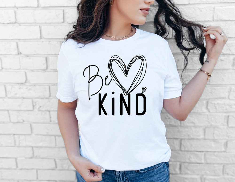 Woman wears Be KIND tee with heart-shaped o, styled with jeans and simple jewelry, embodying Faith Family Designs' trendy, graphic t-shirts ethos.