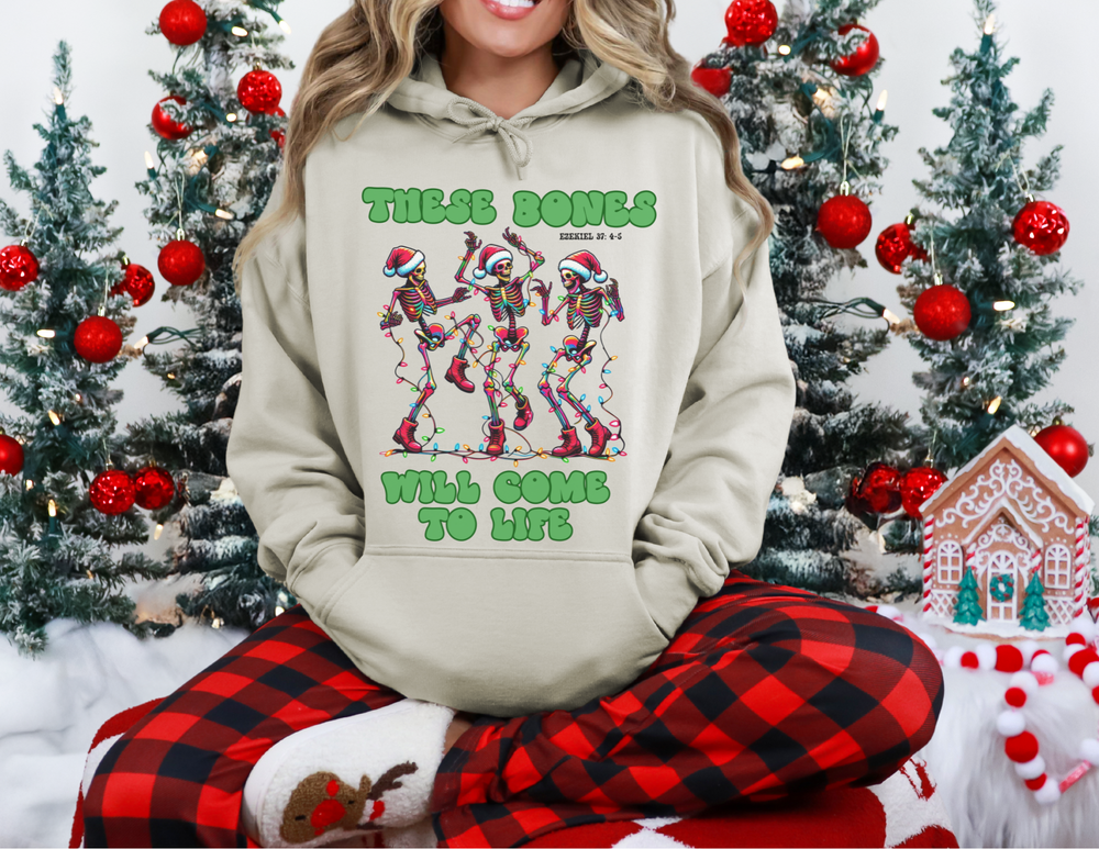 Person wearing the Bones Come to Life hoodie with dancing skeletons, seated in a festive setting with plaid pants and reindeer slippers.