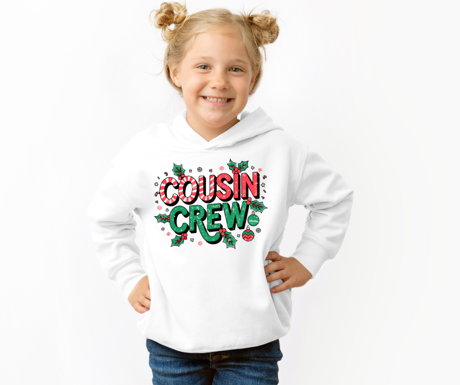 Young girl wearing a Cousin Crew Christmas Toddler Hoodie, featuring festive lettering and accents, designed for comfort and durability with side seam pockets.