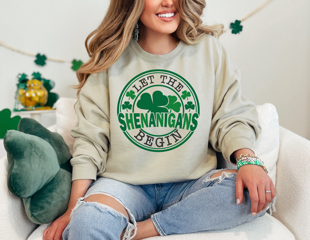Woman on a couch wearing Let the Shenanigans Begin Day Crew sweatshirt, showcasing its comfortable, loose fit and ribbed knit collar detail.