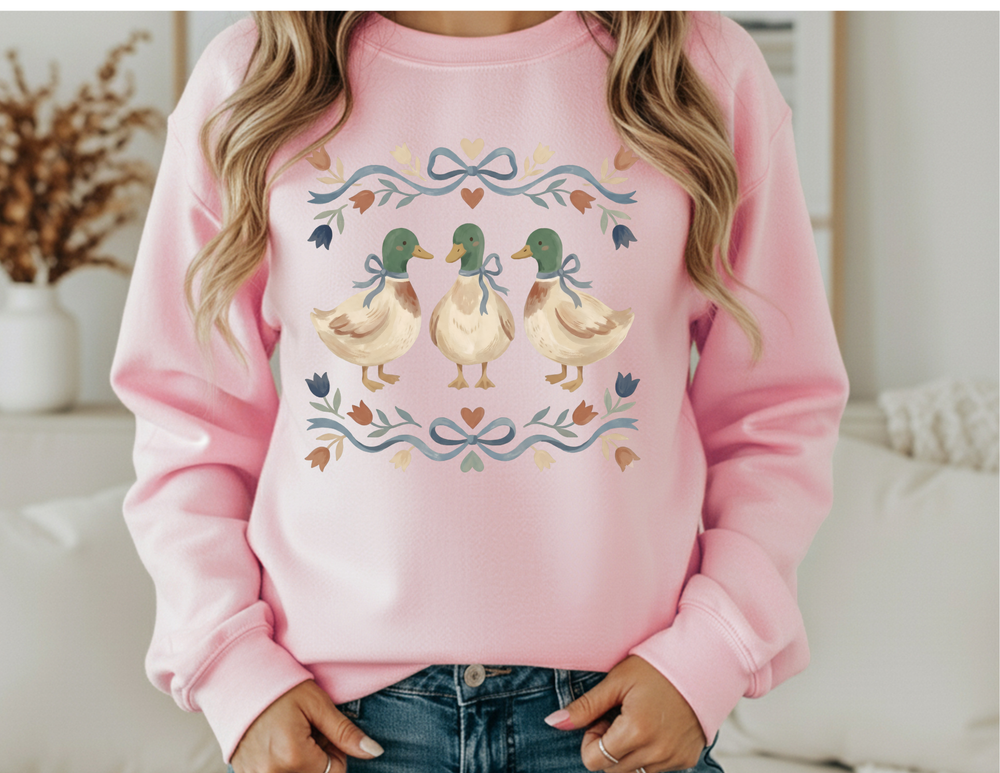 Person wearing light-pink Cottagecore Crew sweatshirt featuring watercolor ducks with blue ribbons, surrounded by pastel floral and heart motifs, emphasizing comfort and style.