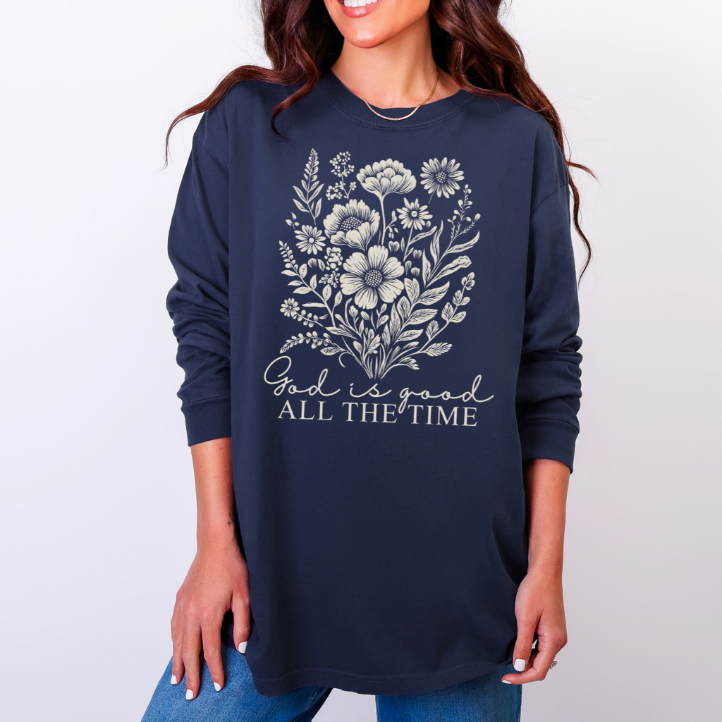 Person wearing a navy-blue God is Good All the Time long-sleeve tee with wildflowers illustration, highlighting comfort and style from Faith Family Designs.