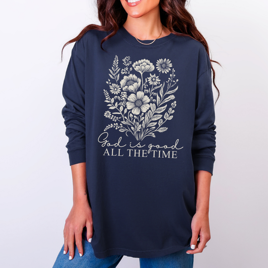 Person wearing a navy-blue God is Good All the Time long-sleeve tee with wildflowers illustration, highlighting comfort and style from Faith Family Designs.