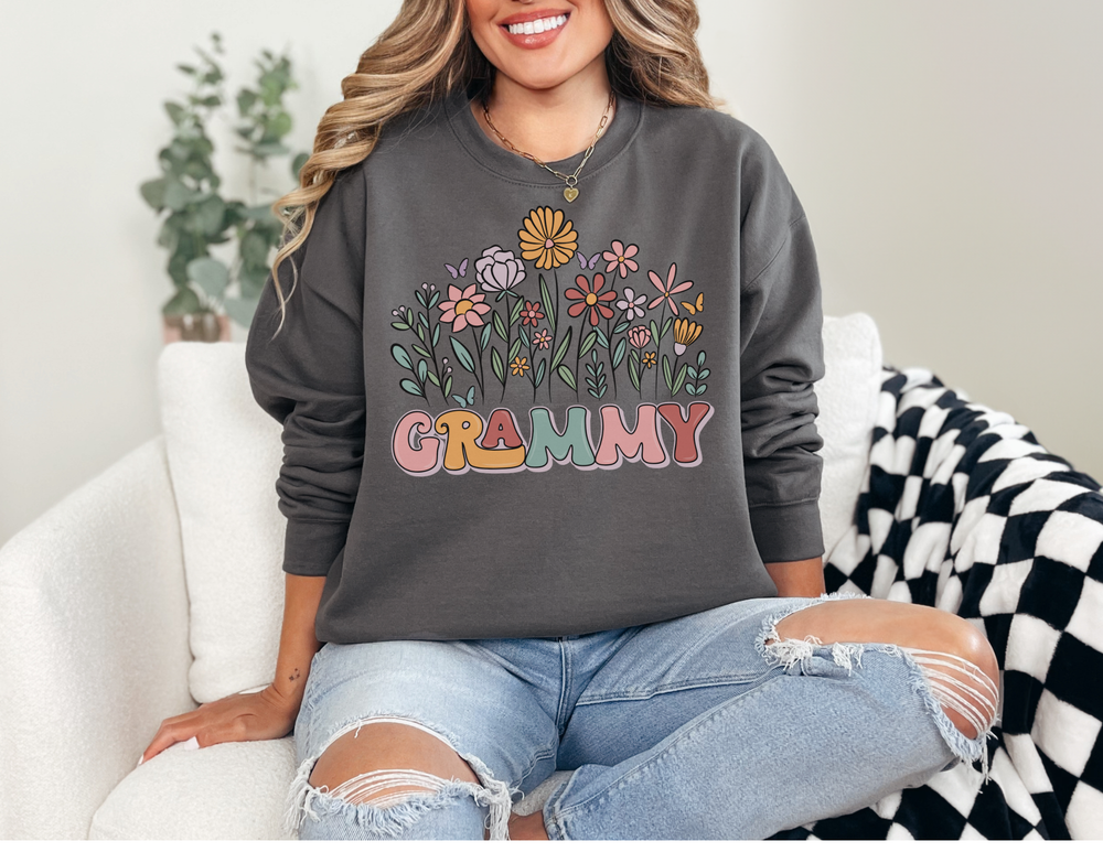 Person in light-wash jeans wearing a “GRAMMY” flower sweatshirt, seated on an armchair, embodying the comfortable and stylish design by Faith Family Designs.
