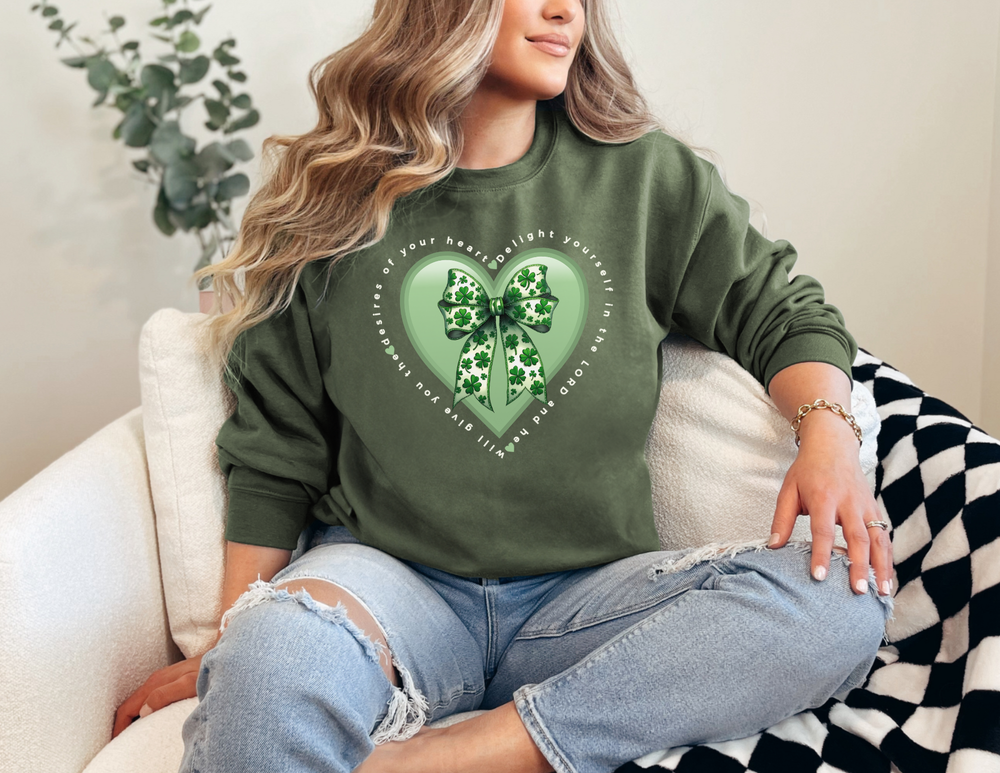 Person wearing Delight in the LORD Long Sleeve Tee with heart graphic and clover bow, seated casually, showcasing its fit and style.