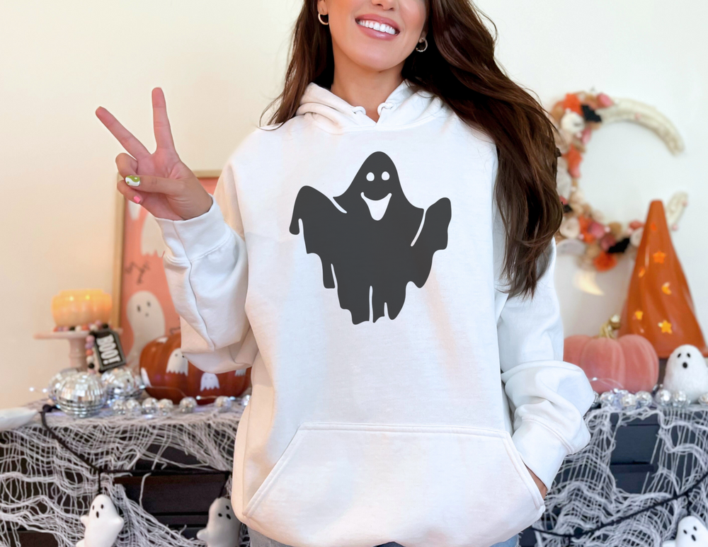 A cozy Ghost Hoodie in white, featuring a black ghost design. Unisex heavy blend with kangaroo pocket and matching drawstring. Ideal for chilly days, made of 50% cotton, 50% polyester.