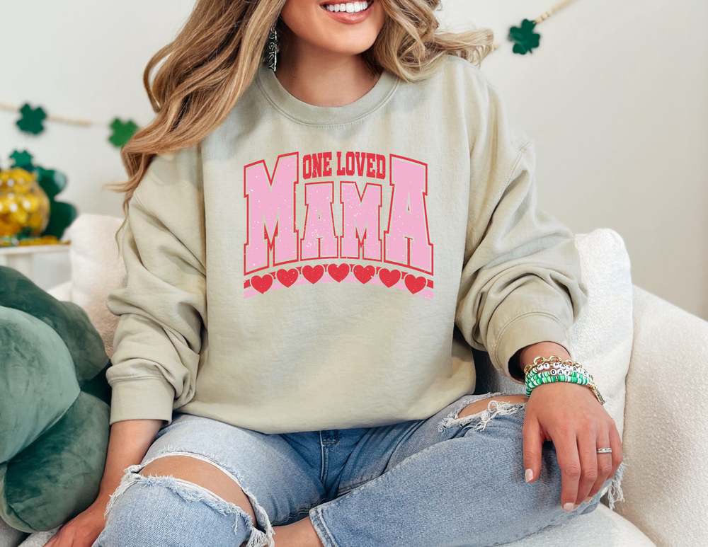 Woman on a couch wearing the One Loved Mama Crew sweatshirt from Worlds Worst Tees, showcasing its comfortable, loose fit and ribbed collar.