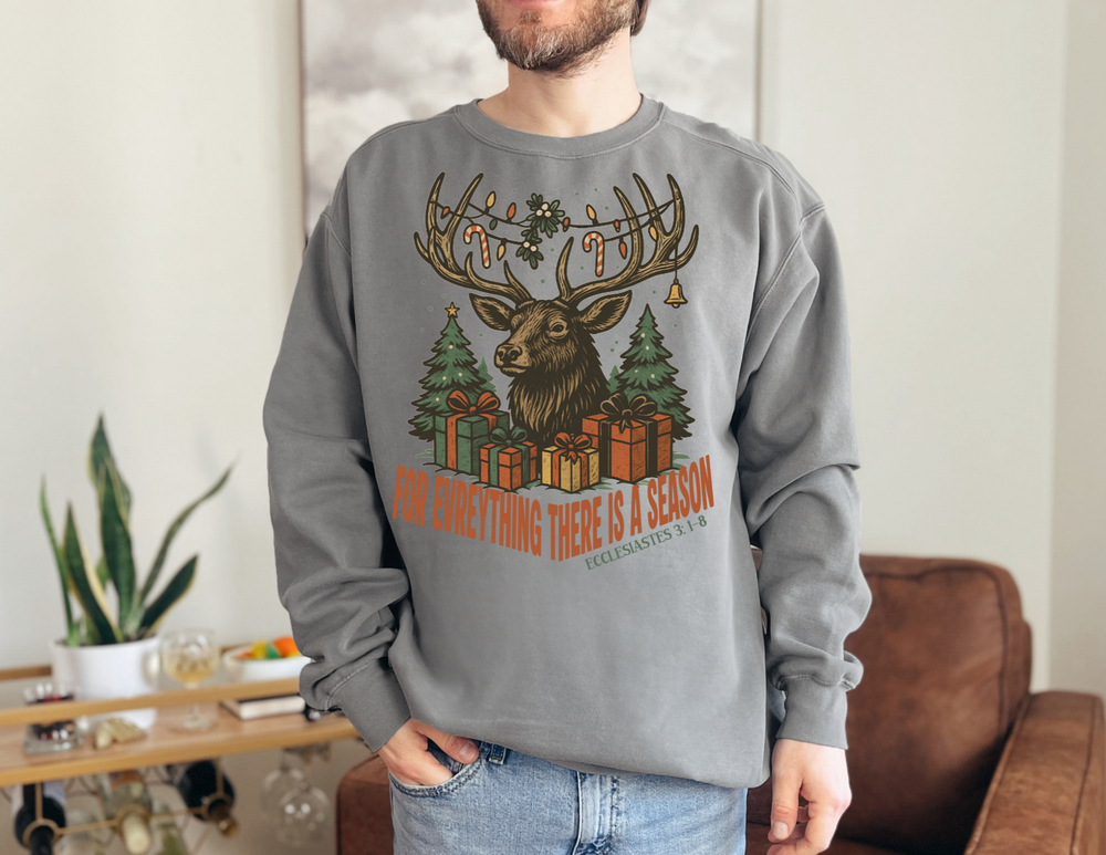 Person wearing For Everything There is a Season Christmas Long Sleeve Tee featuring a stag scene with festive decorations, standing in a cozy living space.
