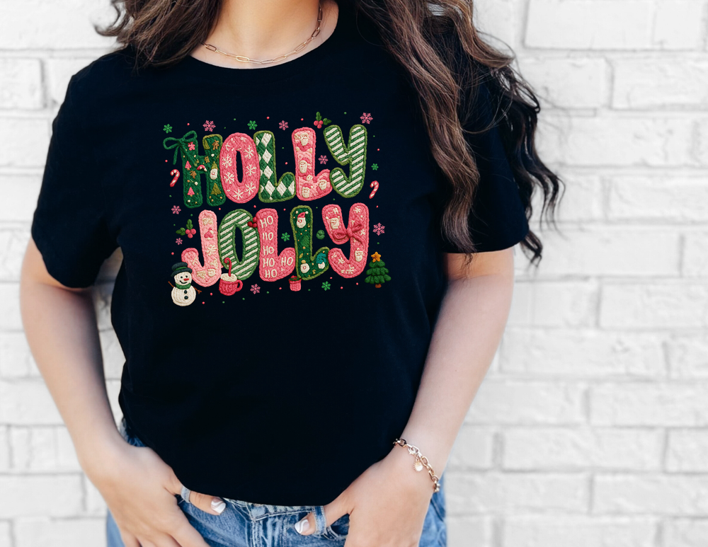 Woman wearing a black Holly Jolly Tee with festive pink and green holiday designs, including snowflakes and holly, paired with blue jeans.