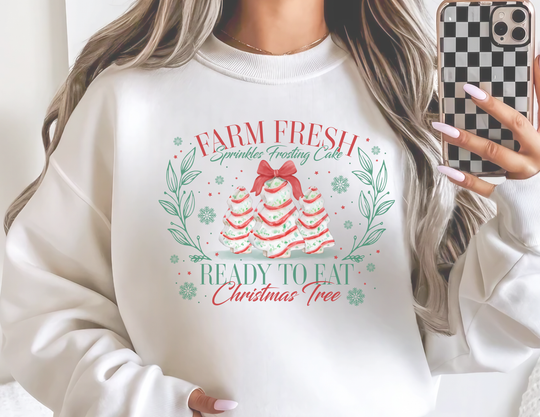 Person in mirror selfie wearing a Farm Fresh Cookies Crew oversized sweatshirt with festive Christmas cake graphics, holding a checkered smartphone case.