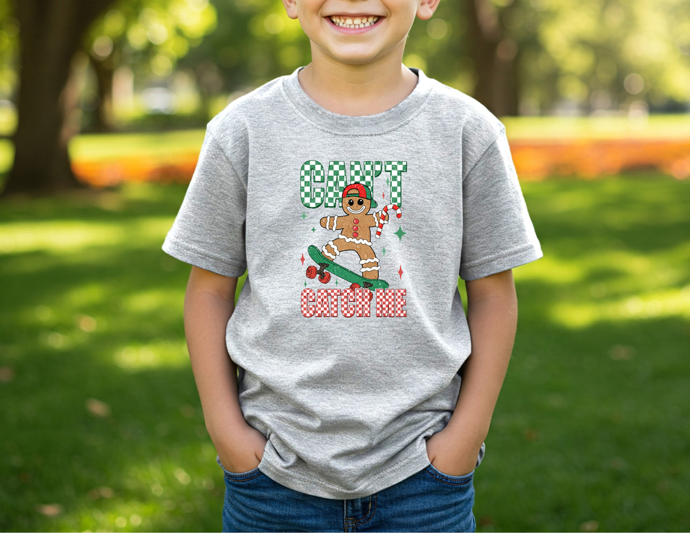 Child wearing Can't Catch Me Kids Tee with a skateboarding gingerbread design, standing in a sunlit park. Perfect for everyday, durable and soft cotton blend.