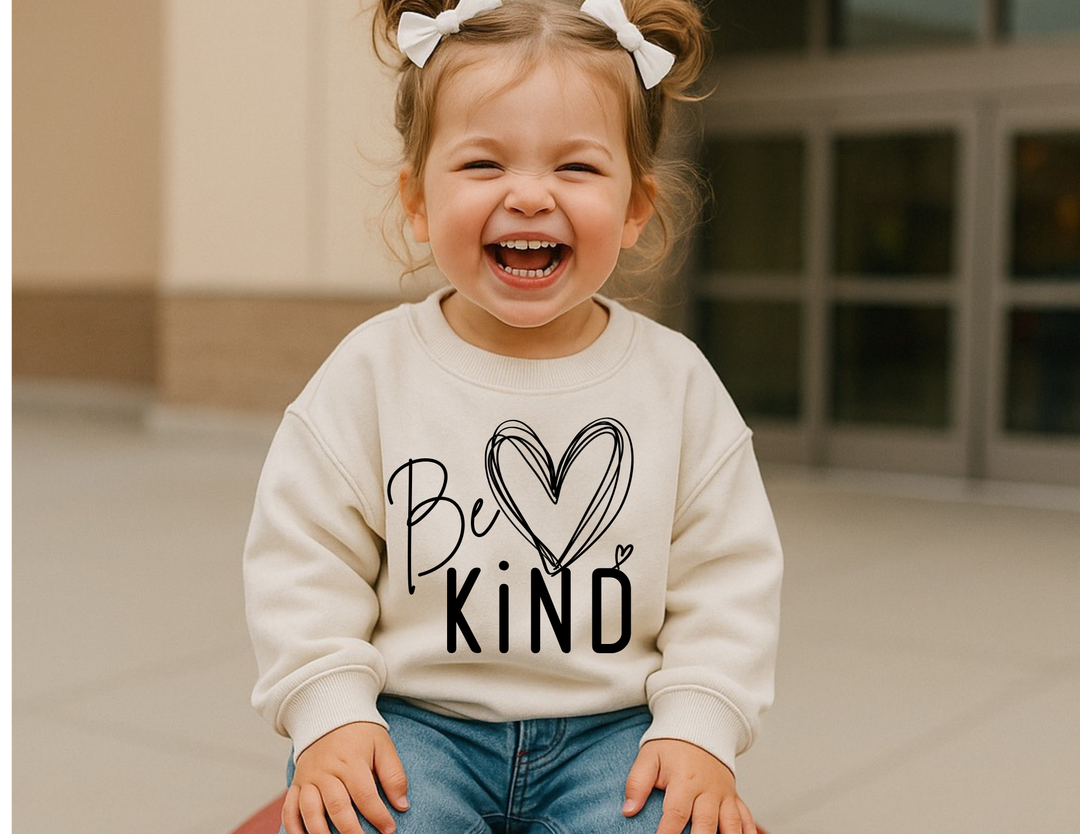 Smiling toddler in Be Kind sweatshirt with pigtails, showcasing the cozy and durable design from Faith Family Designs.