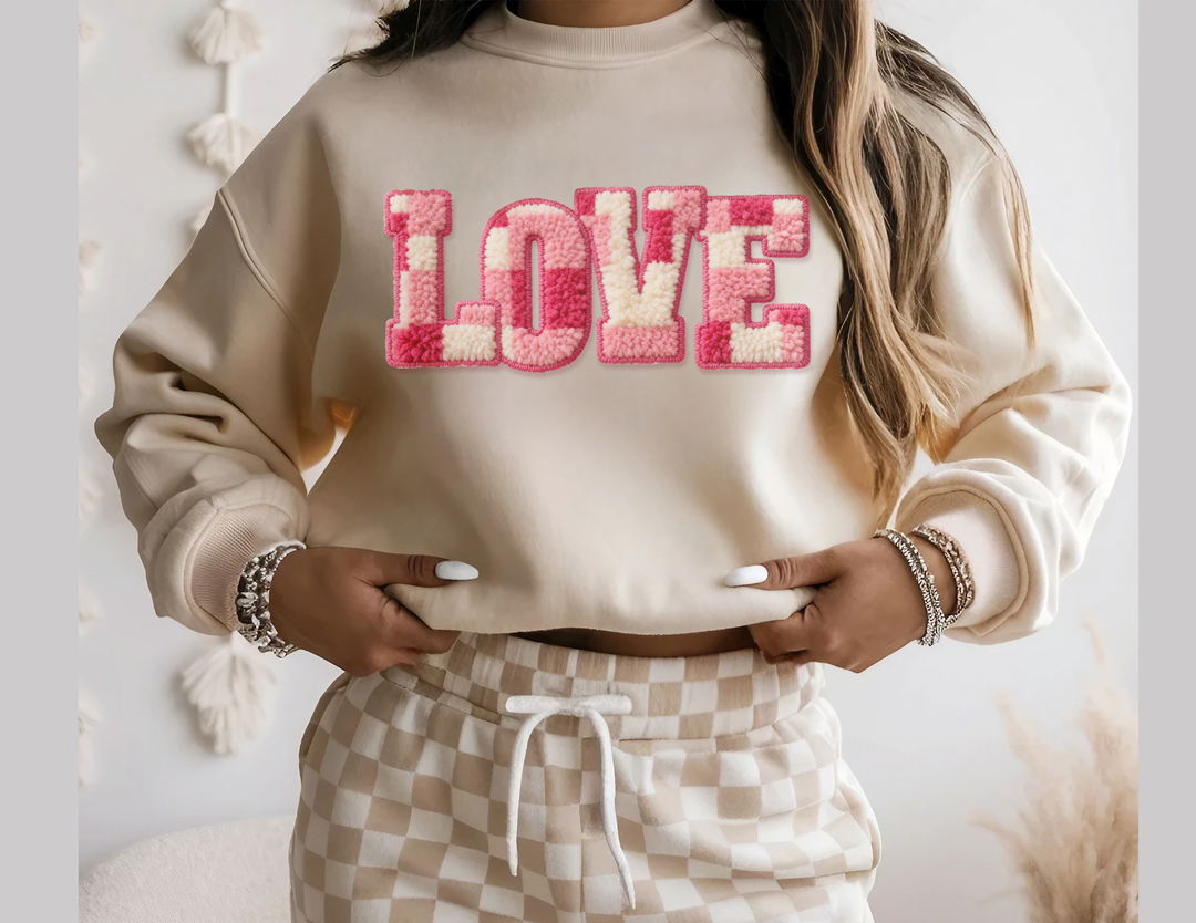 Person wearing Love Crew sweatshirt with chunky tufted letters, paired with high-waisted checker-printed lounge pants, accessorized with layered bracelets.