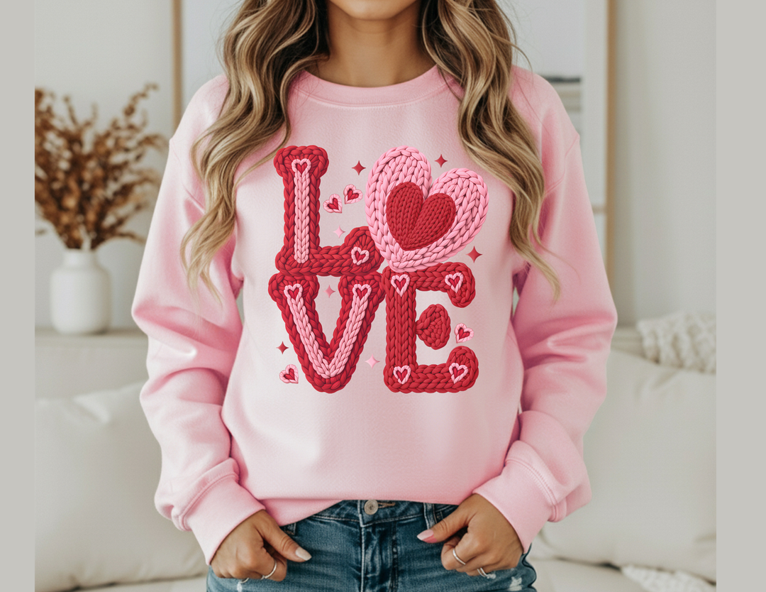 Person wearing Love Heart Crew sweatshirt with LOVE in chunky, braided yarn-style graphic and tiny hearts, paired with blue jeans.