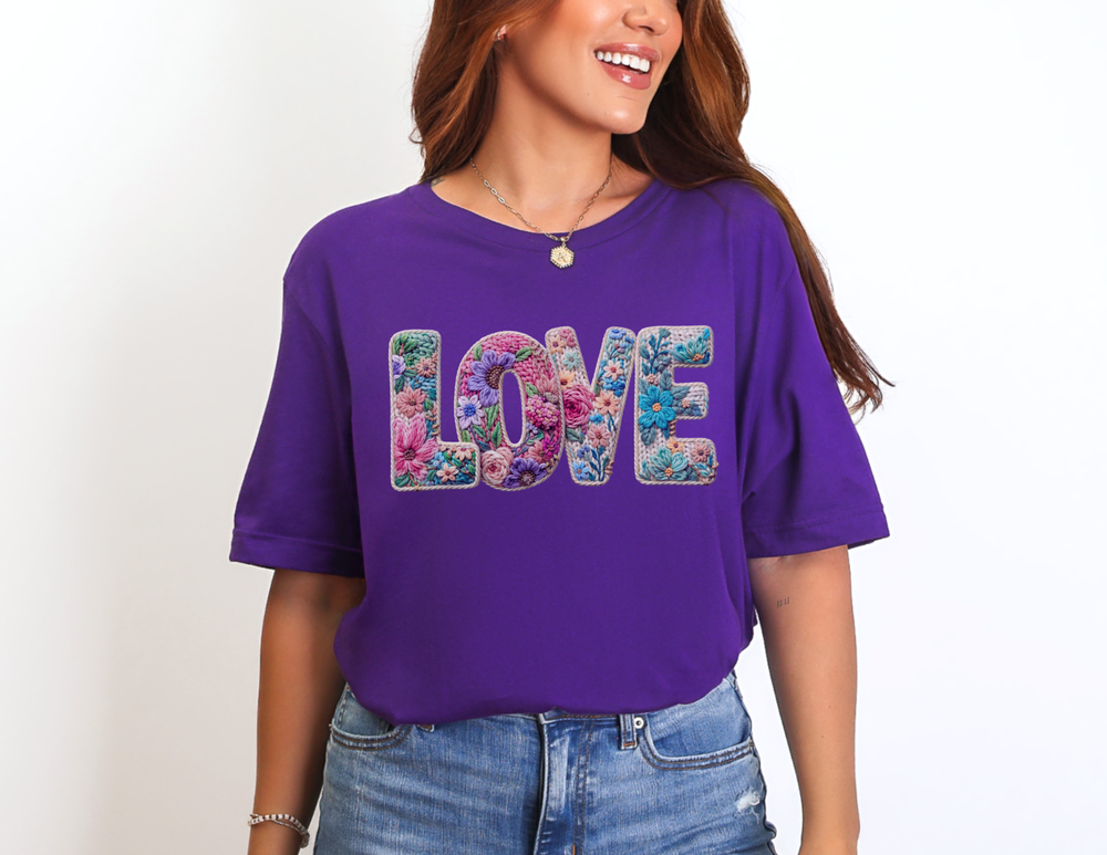 Person wearing vibrant “LOVE” Spring Tee with colorful floral design, paired with denim jeans, necklace, and bracelet, embodying casual, cheerful style.