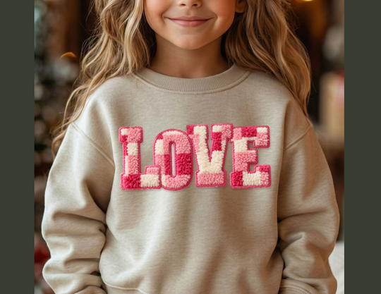 Young child wearing a light-beige LOVE toddler crew sweatshirt with fluffy chenille letters, smiling gently. Ideal for warmth and comfort.