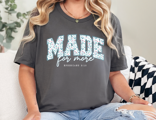 Person wearing MADE for more T-shirt with leaf pattern, light-wash distressed jeans, and gold jewelry, seated on sofa. From Faith Family Designs collection.