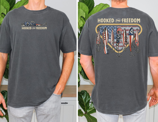 Hooked on Freedom Tee featuring patriotic fishing lures and HOOKED on FREEDOM text on vintage-washed dark-gray, short-sleeve T-shirt, modeled indoors.