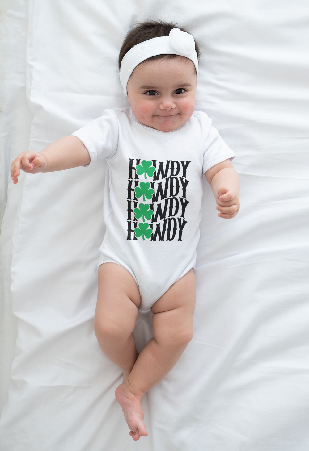 Baby wearing the Howdy Lucky Onesie, made from soft ring-spun cotton, lying on a white sheet with visible lap shoulders for easy adjustments.