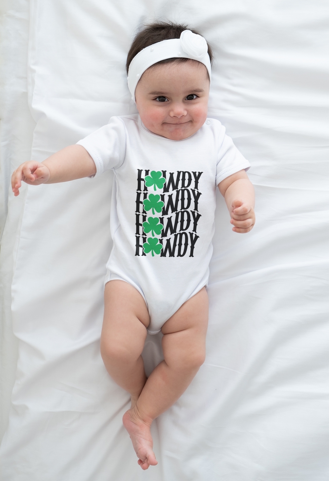 Baby wearing the Howdy Lucky Onesie, made from soft ring-spun cotton, lying on a white sheet with visible lap shoulders for easy adjustments.
