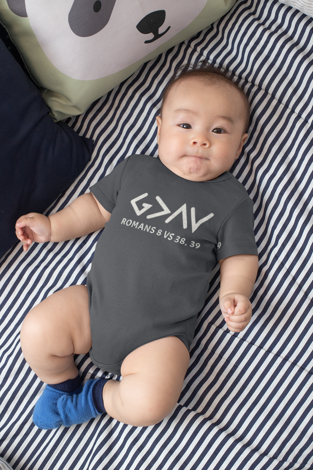 Baby lying on a striped blanket wearing the God is Greater Onesie, showcasing its soft, comfortable fit with lap shoulders for easy dressing.