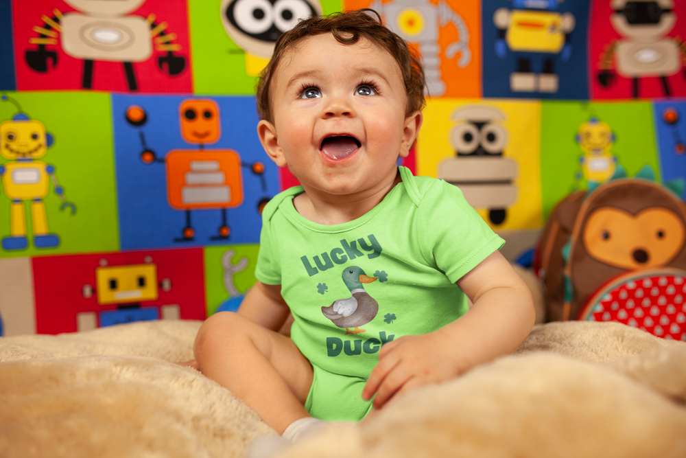 Baby wearing Lucky Duck Onesie with a duck and clover design, sitting on a blanket. The onesie features lap shoulders for easy dressing.