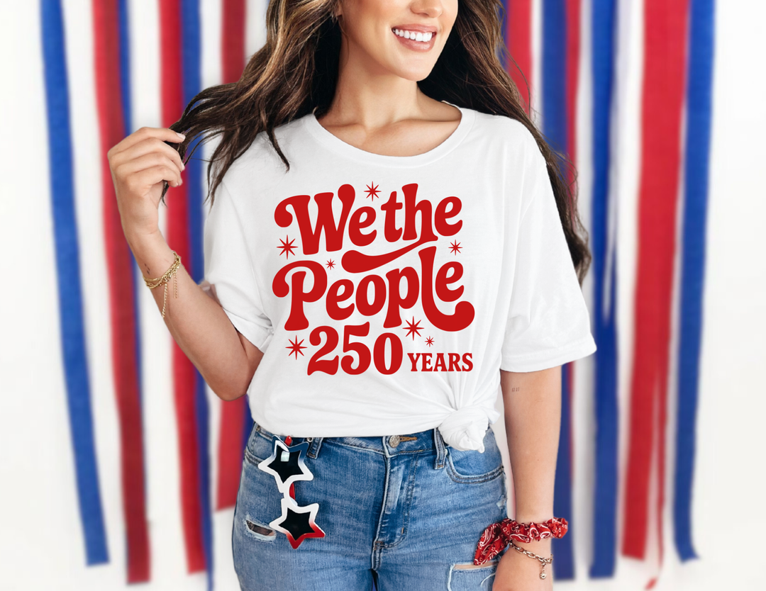 Young woman in We the People 250 Years tee with distressed jeans and star cutouts, showcasing a playful, patriotic style with a red bandana accent.