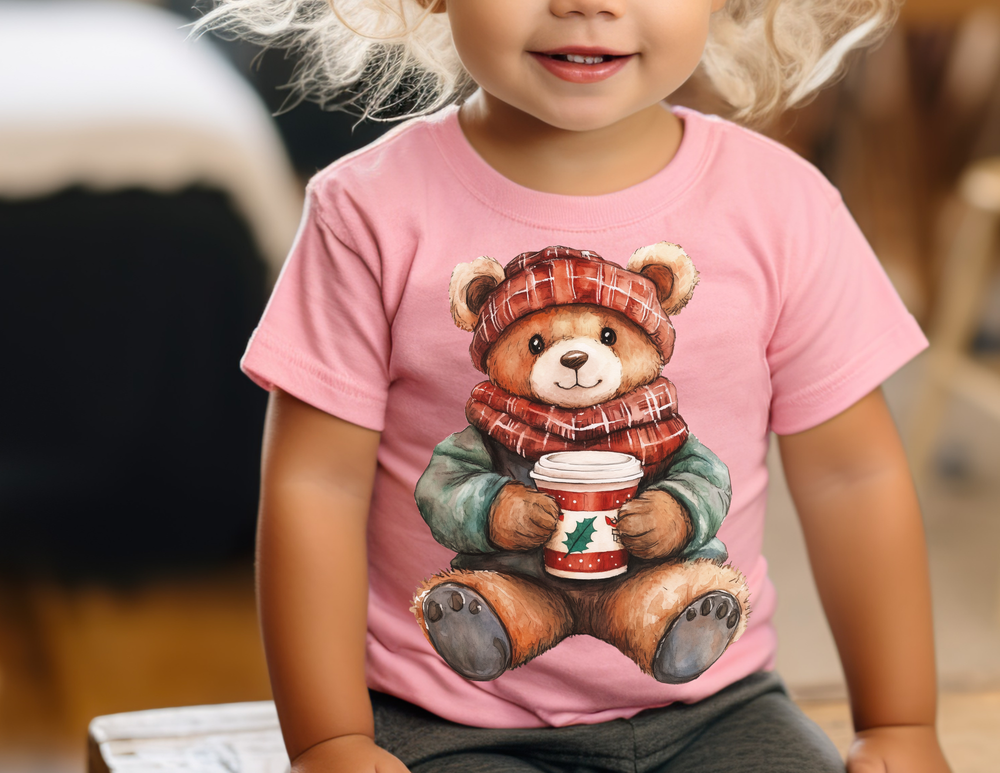 Young child wearing the Old Money Baby Tee featuring a teddy bear with a festive cup, seated indoors, highlighting cozy and stylish comfort for little ones.