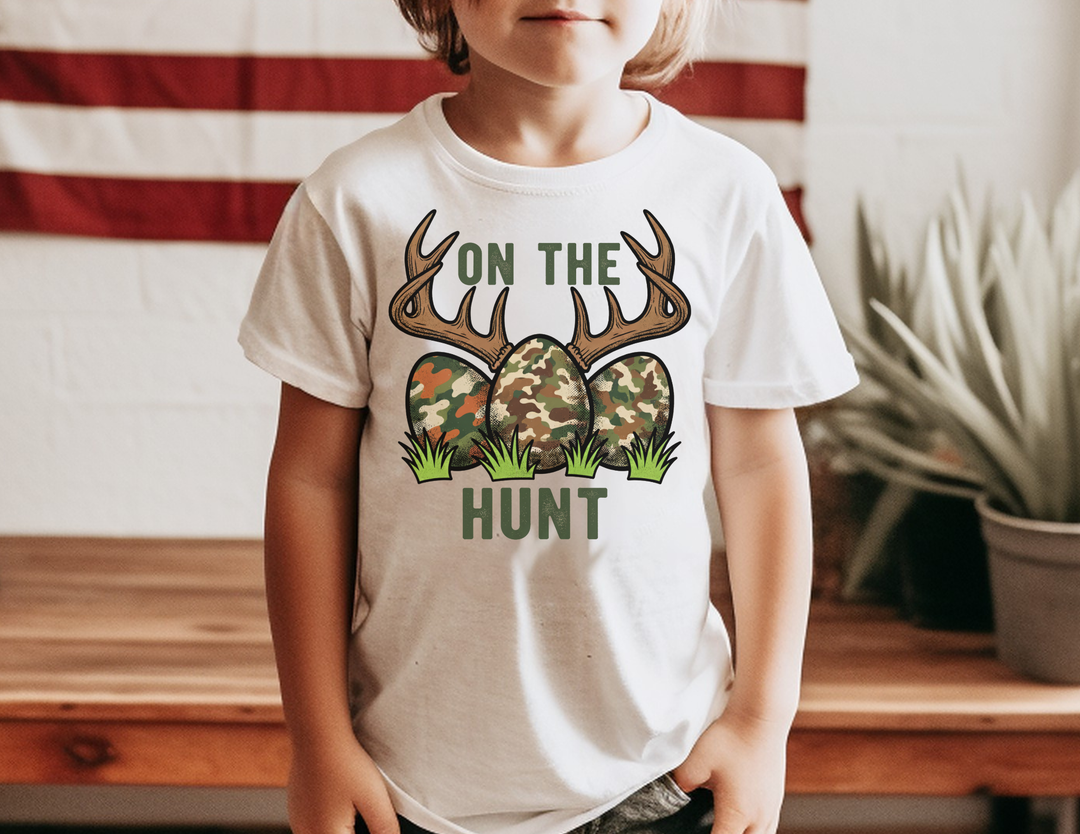 Child wearing the On the Hunt Kids Tee featuring camo eggs and antlers graphic, ideal for everyday use with durable, soft cotton fabric.