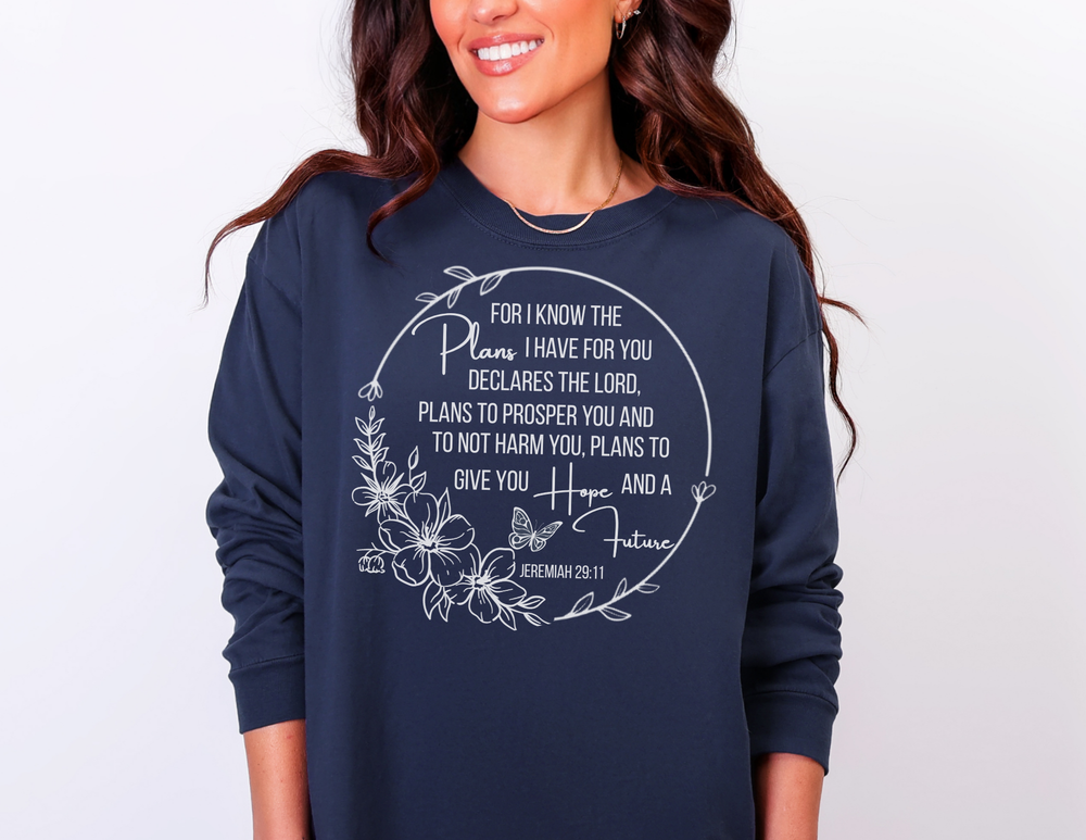 Person wearing navy-blue Plans Hope Future Long Sleeve Tee with floral wreath and Jeremiah 29:11 verse. Comfortable, 100% cotton, relaxed fit sweatshirt.