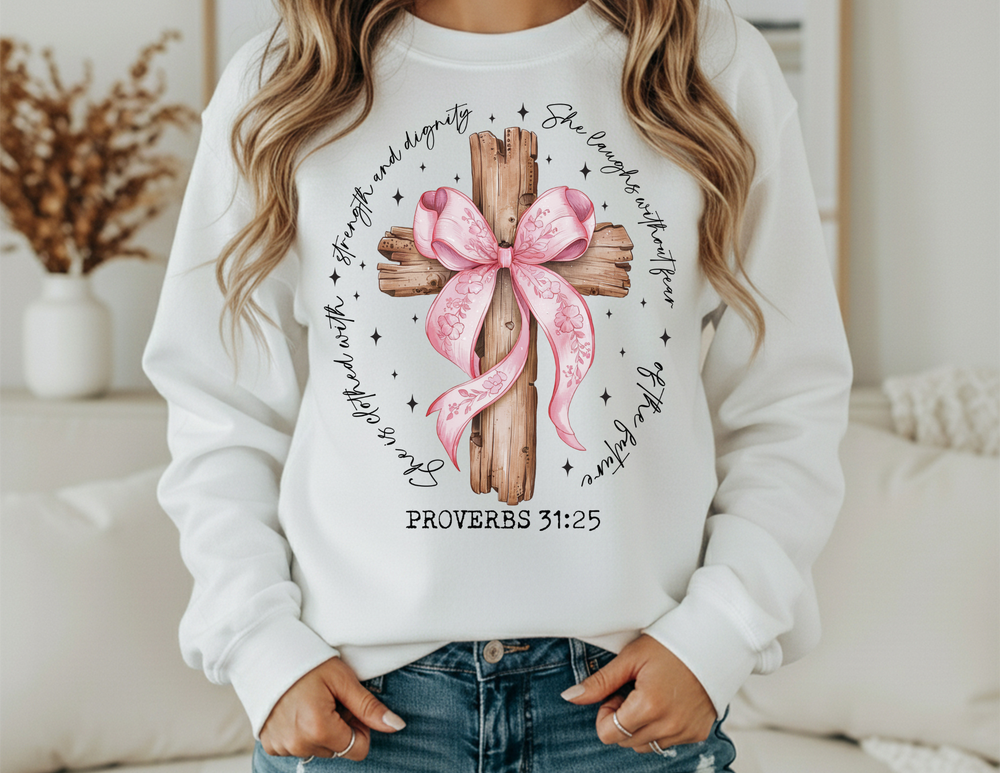 Person wearing a Proverbs 31:25 Crew sweatshirt featuring a rustic wooden cross with pink ribbon and hand-lettered verse, paired with blue jeans.