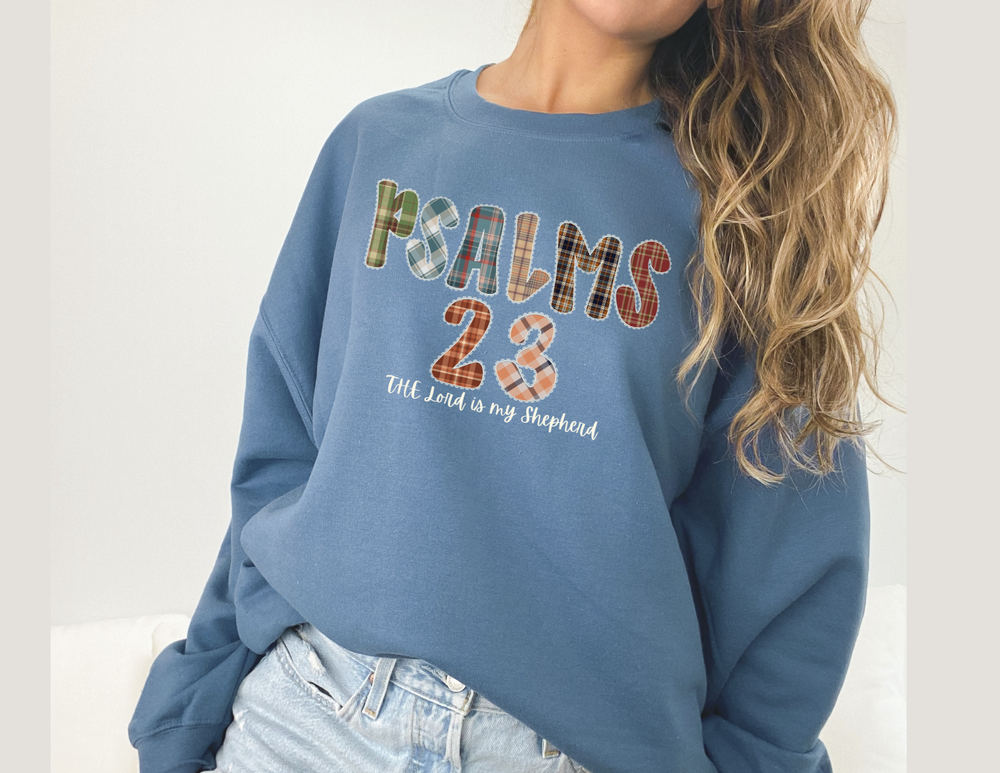 Person wearing a slate-blue Psalms 23 hoodie with plaid lettering and The Lord is my Shepherd, paired with light-wash jeans.