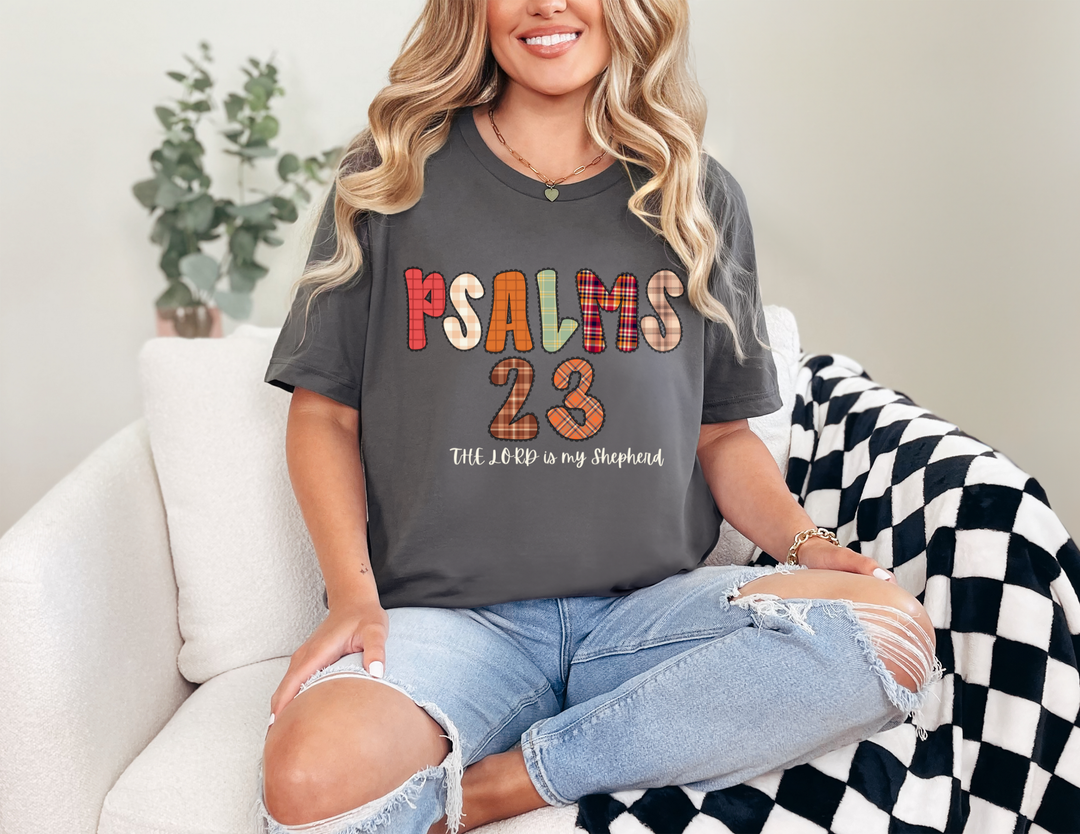 Woman on sofa wearing Psalms 23 graphic tee, dark gray, with The Lord is My Shepherd text; paired with light-wash, ripped jeans.