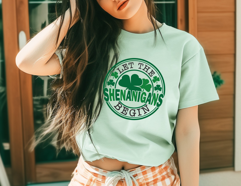 Woman wearing 'Let The Shenanigans Begin Tee', a classic unisex jersey short sleeve t-shirt, posing casually. The tee features ribbed knit collars and dual side seams for durability.