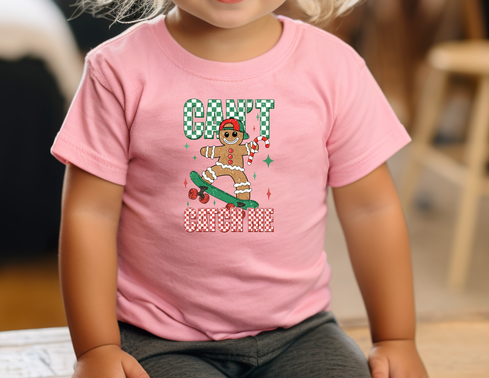 Young child wearing the Can't Catch Me Baby Tee with a gingerbread man design, emphasizing style and comfort for first steps in a soft, durable cotton fabric.