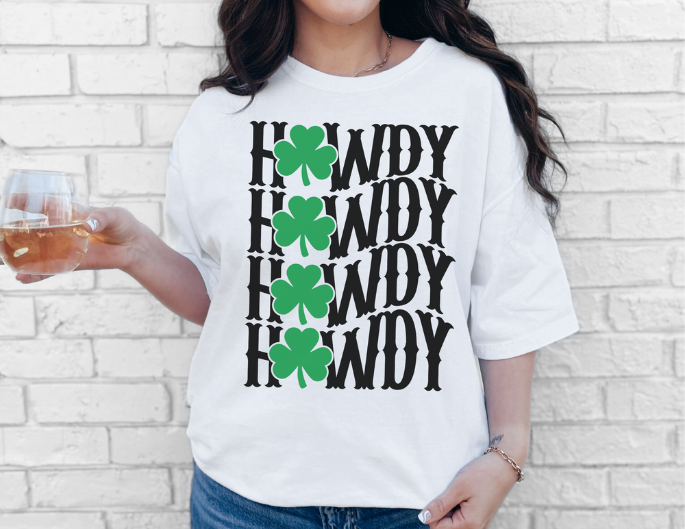Woman wearing the Howdy Lucky Tee, a white t-shirt with black text and green clovers, holding a glass of beer, showcasing casual style.