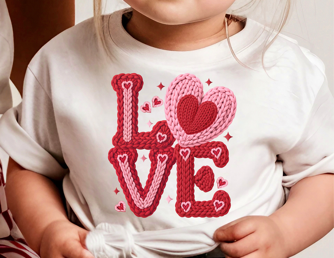 Young child wearing the Love Heart Toddler Tee, featuring a colorful LOVE graphic with a heart design, showcasing softness and durability ideal for toddlers.