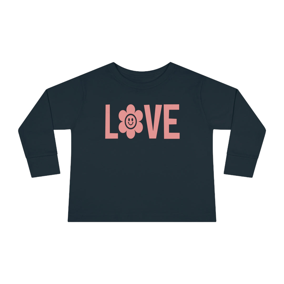 A Love Toddler Long Sleeve Tee featuring a pink flower and a smiling face design on a blue shirt. Made of durable 100% combed ringspun cotton, with a ribbed collar for comfort. Toddler unisex fit for lasting wear.