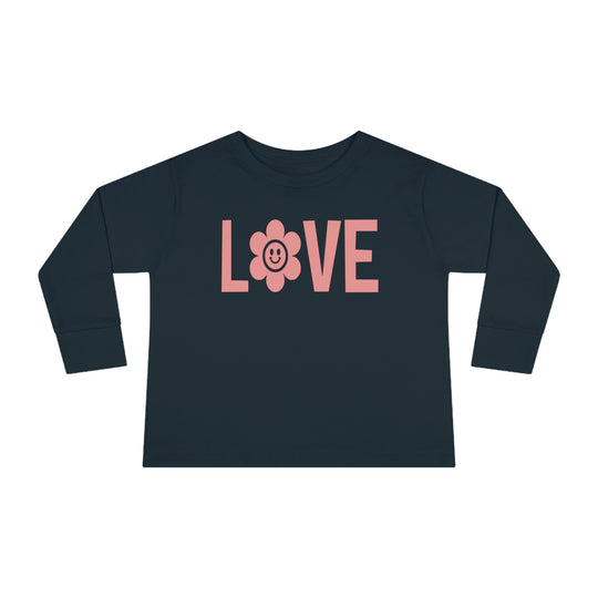 A Love Toddler Long Sleeve Tee featuring a pink flower and a smiling face design on a blue shirt. Made of durable 100% combed ringspun cotton, with a ribbed collar for comfort. Toddler unisex fit for lasting wear.