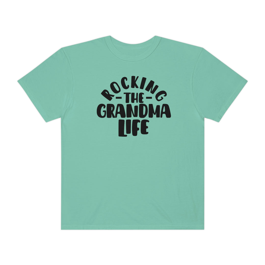 A cozy Rocking the Grandma Life Tee in green with black text. Made of 100% ring-spun cotton, featuring a relaxed fit and durable double-needle stitching for everyday comfort.