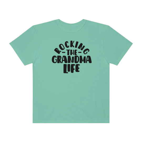 A cozy Rocking the Grandma Life Tee in green with black text. Made of 100% ring-spun cotton, featuring a relaxed fit and durable double-needle stitching for everyday comfort.