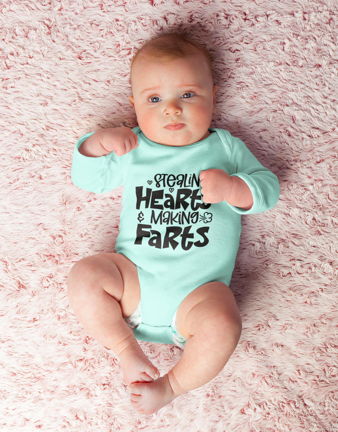 Infant fine jersey bodysuit featuring Stealin Hearts and Making Farts Onesie. 100% cotton fabric, ribbed knit bindings, plastic snaps at closure. Baby lying on pink blanket. Human face, toddler, baby clothing.
