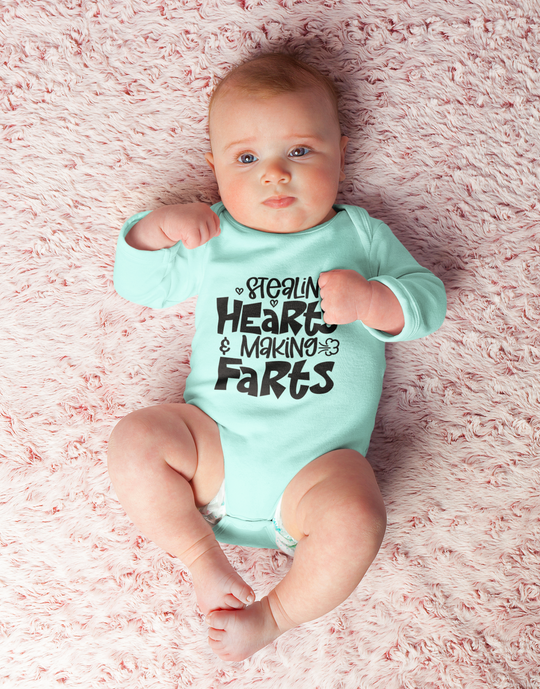 Infant fine jersey bodysuit featuring Stealin Hearts and Making Farts Onesie. 100% cotton fabric, ribbed knit bindings, plastic snaps at closure. Baby lying on pink blanket. Human face, toddler, baby clothing.