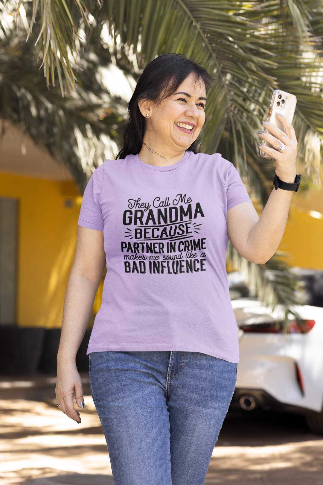 A woman in a purple shirt taking a selfie with a phone, showcasing the They Call Me Grandma Tee. Garment-dyed, ring-spun cotton tee with a relaxed fit and durable double-needle stitching.